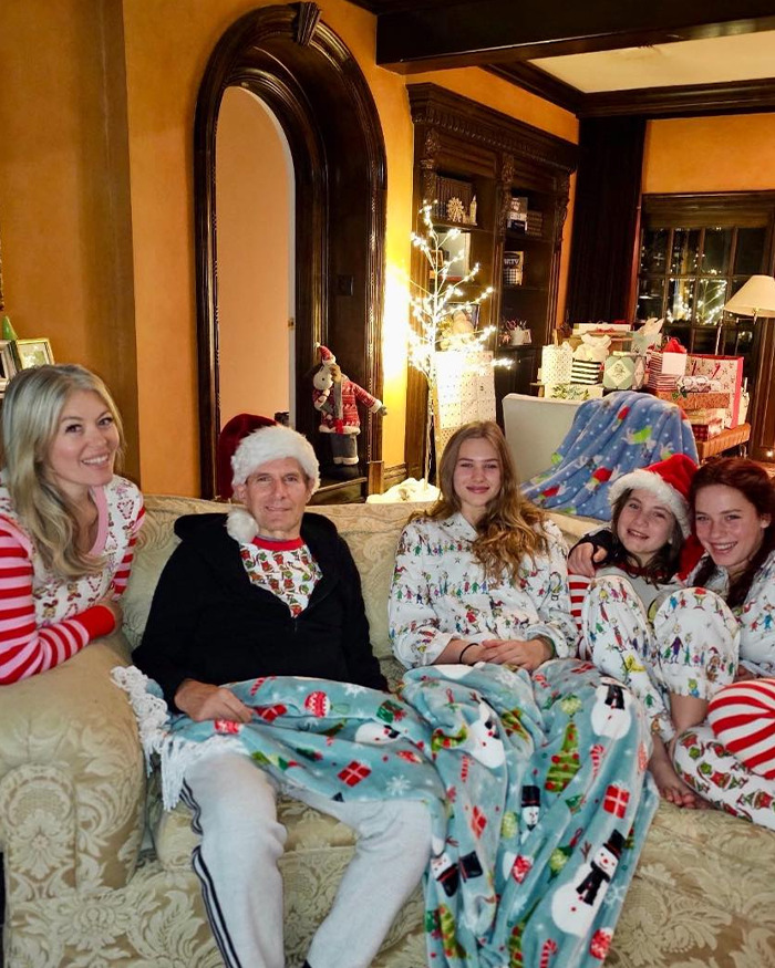 Michael Bolton wearing a Santa hat with family in festive pajamas, seated on a couch during a Christmas celebration.