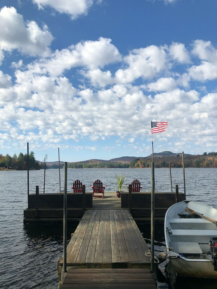 Lake dock with red chairs, an American flag, and a boat under a partly cloudy sky, reflecting rich travel complaints.