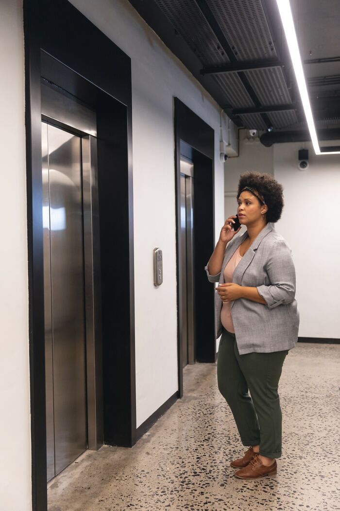 Woman standing near elevator talking on phone in hallway, related to unusual ways people died stories.