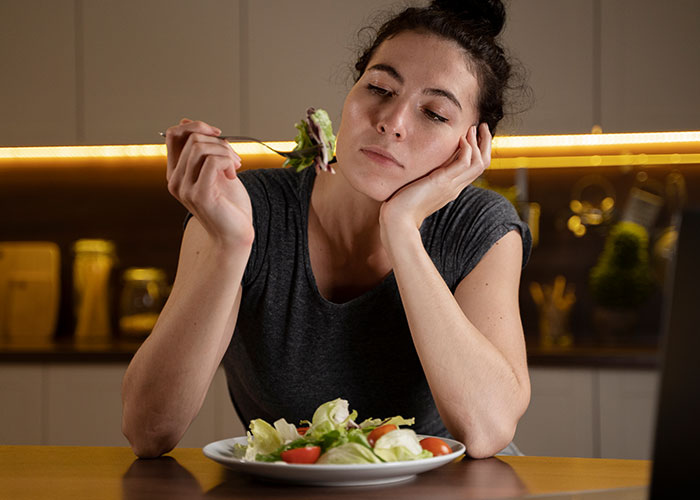 Woman looking upset while eating salad, illustrating conflict with MIL trying to purposely trigger her allergies. Woman looking upset while eating salad, illustrating conflict with MIL trying to purposely trigger her allergies.