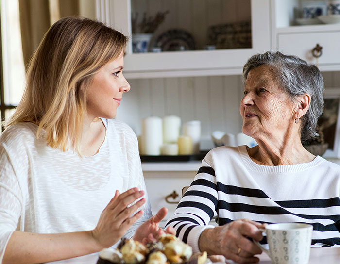 Young woman talking to an older woman in a kitchen, illustrating cheap MIL feeding spoiled food and bullying them to eat it.