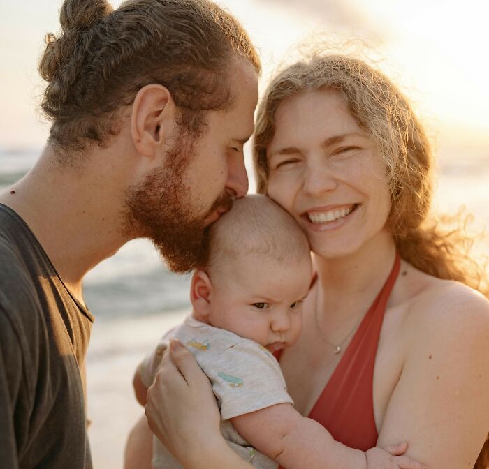 Family with newborn baby at the beach, capturing moments as MIL and SIL plan to see the baby secretly.