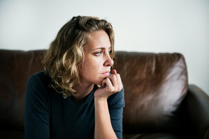 A new mom sitting on a couch, looking pensive and baffled over a secret operation to see the newborn baby.