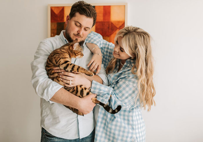 Couple holding and admiring their Bengal cat indoors, highlighting the relationship between pet and owners.