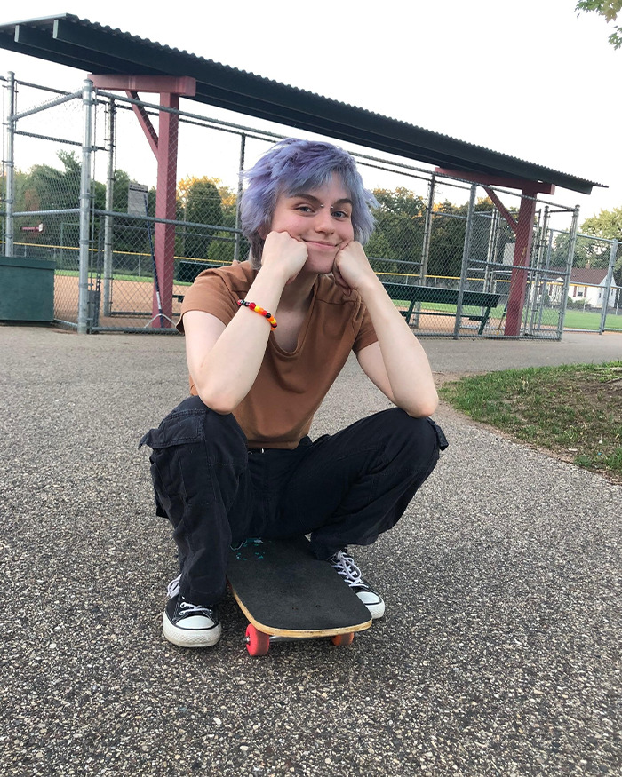 Young person with purple hair sitting on a skateboard at a park, linked to Minneapolis suspect furry girlfriend report