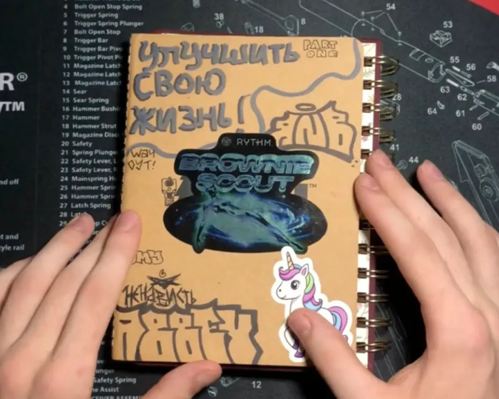 Hands holding a journal with stickers and drawings, related to Minneapolis suspect furry girlfriend and disturbing entries.