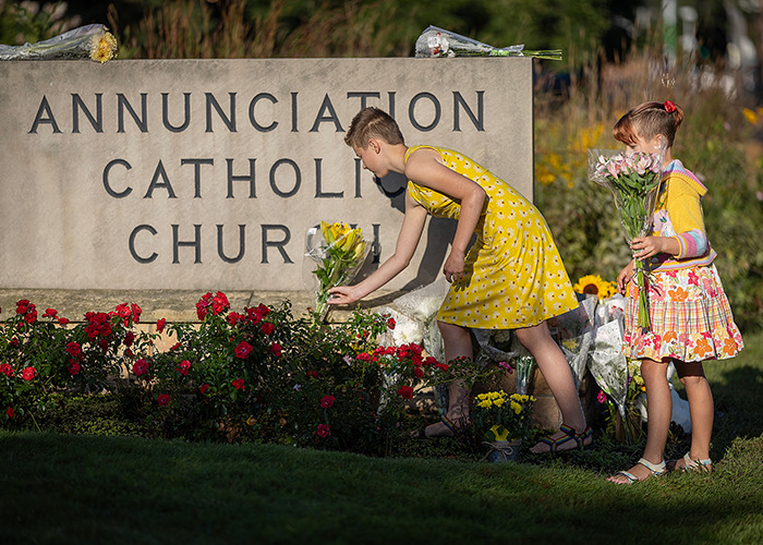 Two girls placing flowers at Annunciation Catholic Church, related to Minneapolis suspect's furry girlfriend and journal entries.