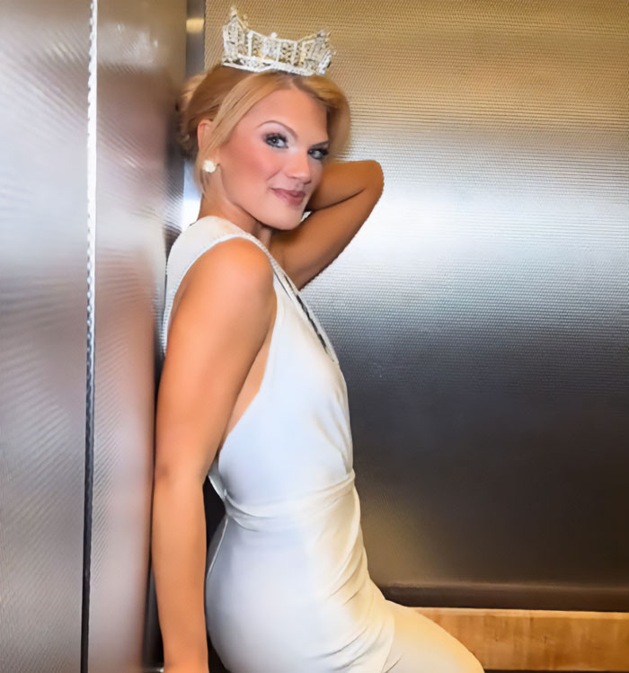Miss America wearing a crown and white dress, posing confidently after winning amid backlash over her look.