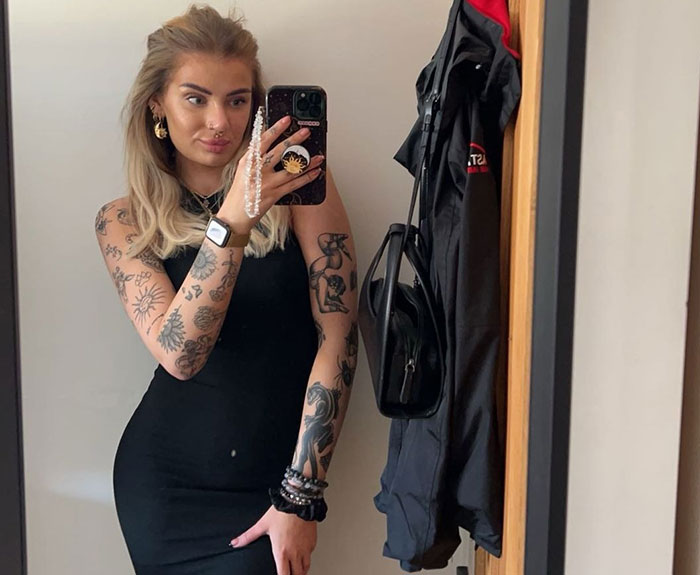 Young woman with tattoos taking a mirror selfie in a black dress, highlighting male co-workers placing bets and legal action. Young woman with tattoos taking a mirror selfie in a black dress, highlighting male co-workers placing bets and legal action.