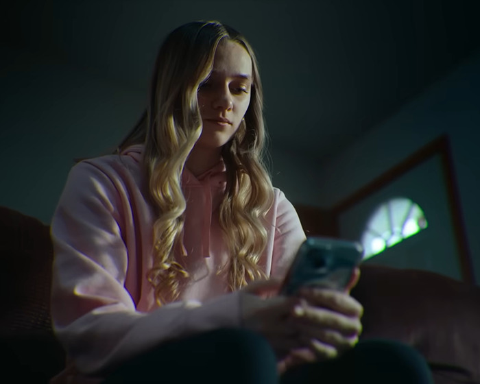 Teen girl in a pink hoodie looking at her phone, highlighting the impact of psychological expert insights on online bullying cases. Teen girl in a pink hoodie looking at her phone, highlighting the impact of psychological expert insights on online bullying cases.
