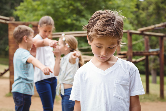 Young boy looking down sadly while other children point and laugh, highlighting family bonding and emotional conflict. Young boy looking down sadly while other children point and laugh, highlighting family bonding and emotional conflict.