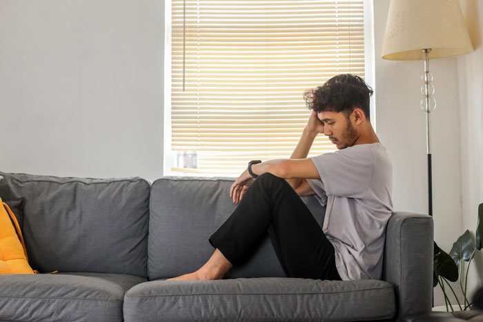 Young man sitting on couch looking upset, reflecting on refusal to care for disabled daughter request from mom. Young man sitting on couch looking upset, reflecting on refusal to care for disabled daughter request from mom.