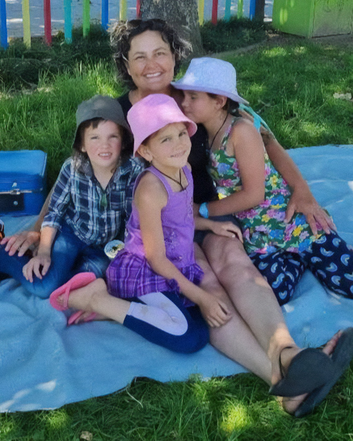 Mom of 3 missing kids sitting outdoors on a blanket with her children on a sunny day in a park setting.