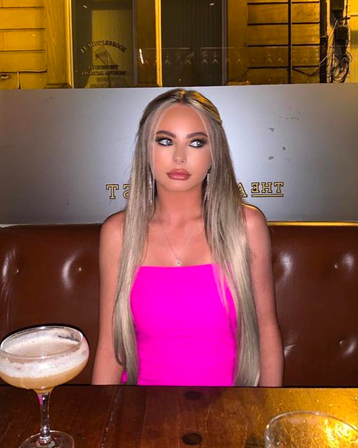 Woman in a bright pink dress seated at a wooden table with drinks, representing mom of student jailed for life in Dubai Woman in a bright pink dress seated at a wooden table with drinks, representing mom of student jailed for life in Dubai