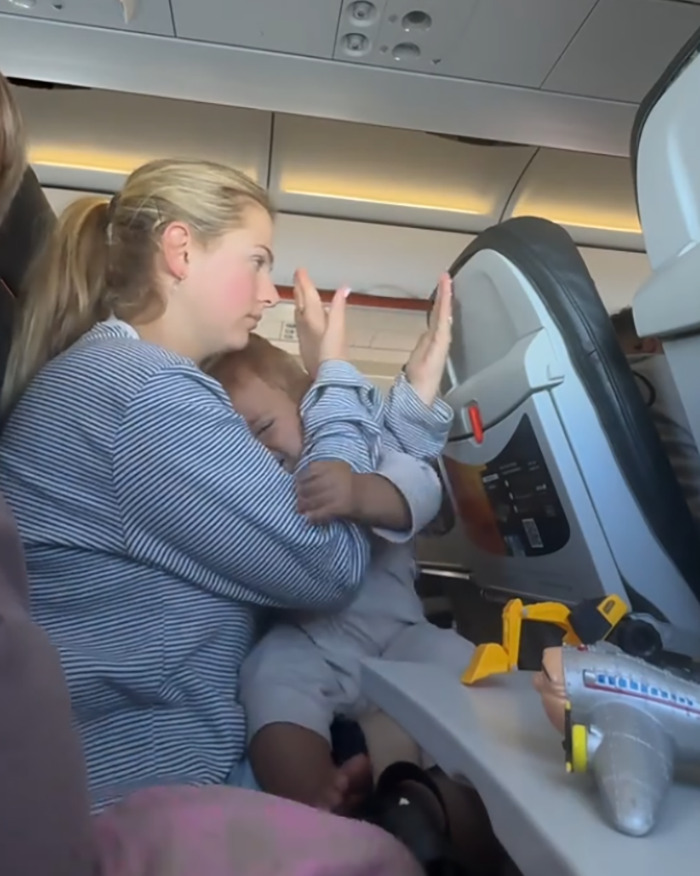 Mom and child reacting to reclined plane seat intruding into their space during a flight, sparking a viral debate. Mom and child reacting to reclined plane seat intruding into their space during a flight, sparking a viral debate.