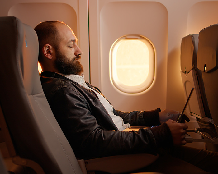 Man sitting in a reclined plane seat using a tablet, illustrating space issues causing annoyance on flights. Man sitting in a reclined plane seat using a tablet, illustrating space issues causing annoyance on flights.