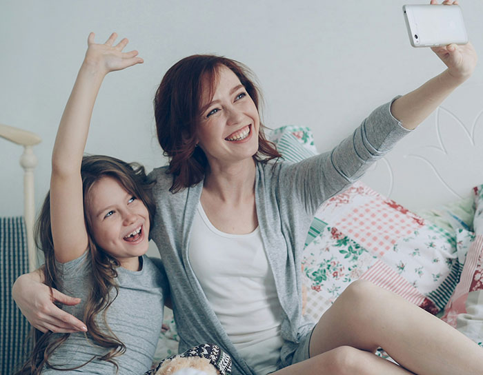A smiling TikTok mom and her child taking a selfie together on a bed with colorful pillows.