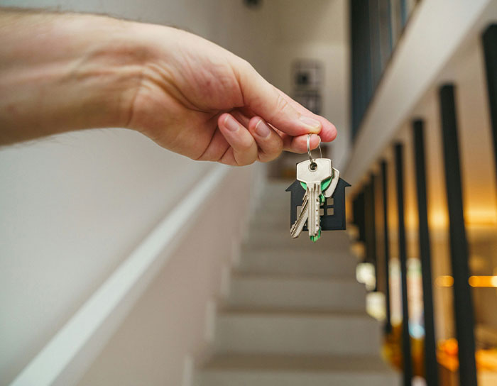 Hand holding house keys inside a modern home, illustrating professions tied to TikTok moms and disliked jobs.