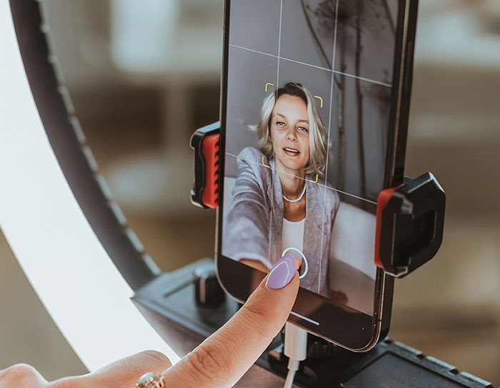 Woman recording TikTok video on smartphone with ring light, illustrating TikTok moms creating online content.
