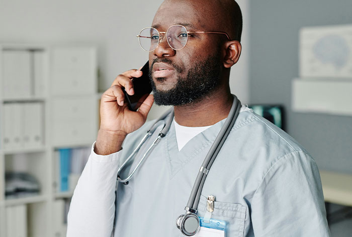 Healthcare professional wearing scrubs and glasses, using phone in office, representing hated professions discussed by TikTok Moms.