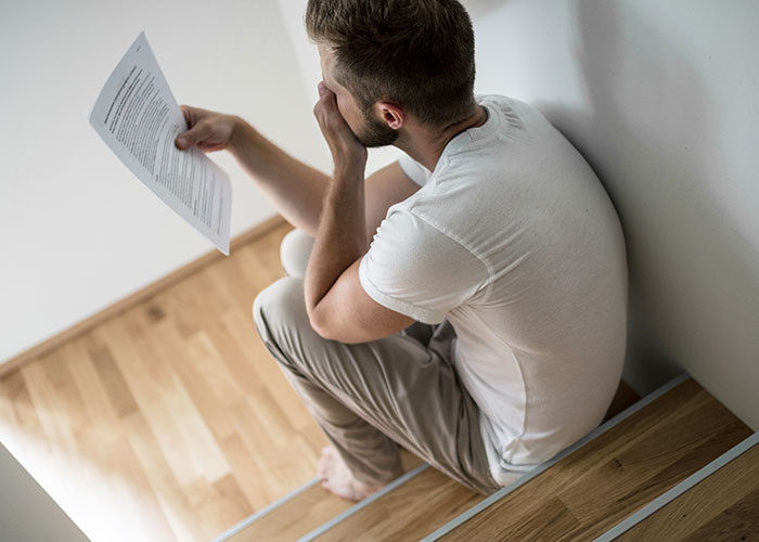 Young man sitting on stairs holding a letter, appearing upset about college acceptance and hidden news from mom.