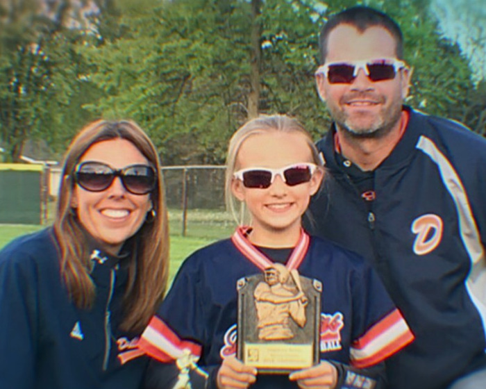 Family posing outdoors with a young girl holding a trophy, related to mom anonymously bullying daughter story.