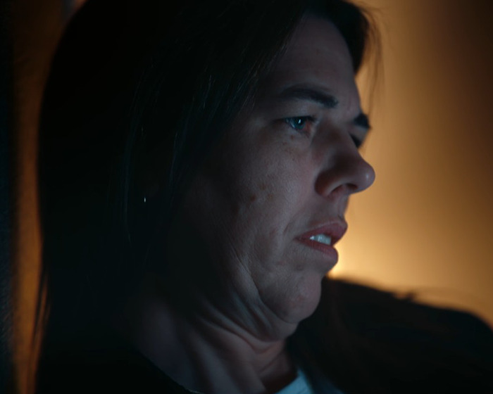 Woman in dim light with a serious expression, reflecting on anonymous bullying and a shocking confession moment.