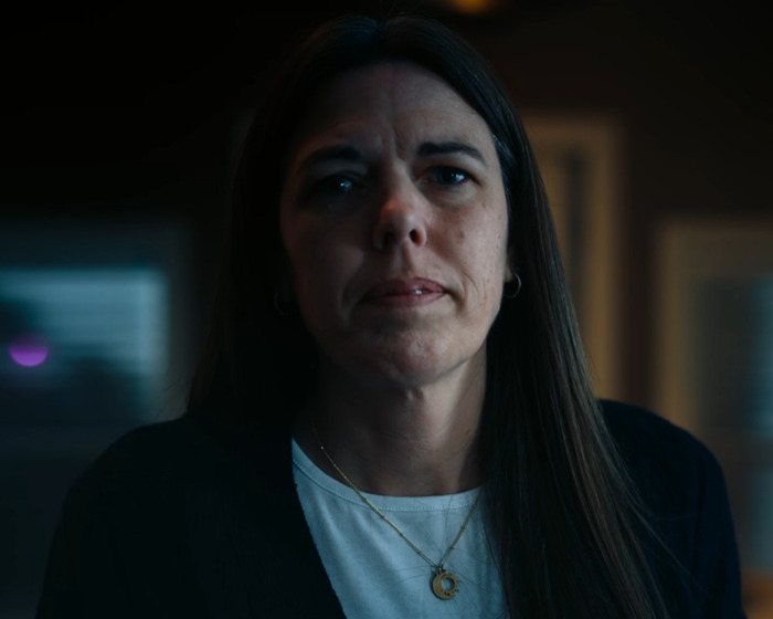 Woman with long dark hair and a serious expression in a dimly lit room, representing anonymous bullying by mom.
