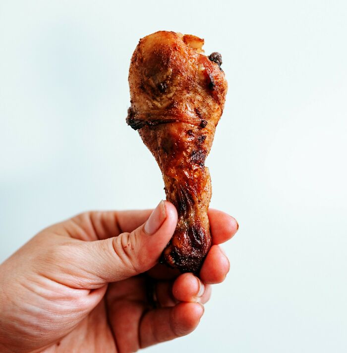 Hand holding a grilled chicken drumstick representing unholy health violations in restaurants inspectors witnessed.