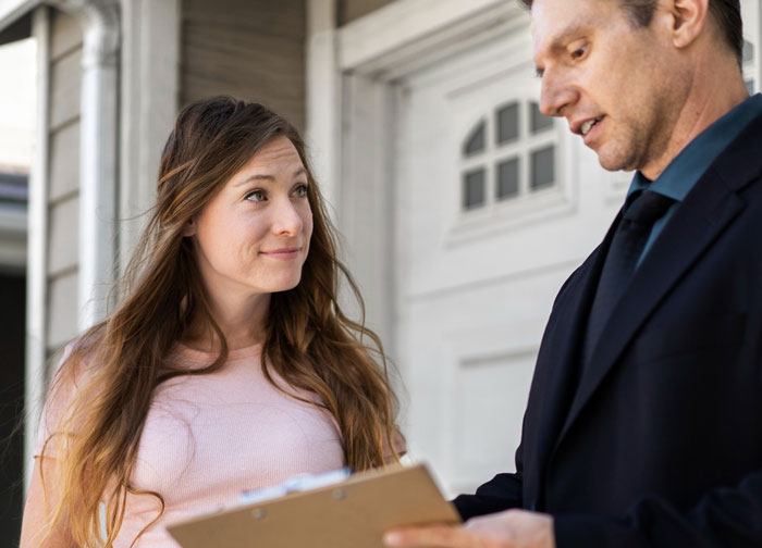 Neighbor upset speaks with nanny holding clipboard near front home, discussing parking issues and concerns outside.