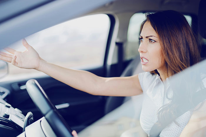 Nurse frustrated inside car after a long shift, reacting angrily to neighbor using her driveway again.