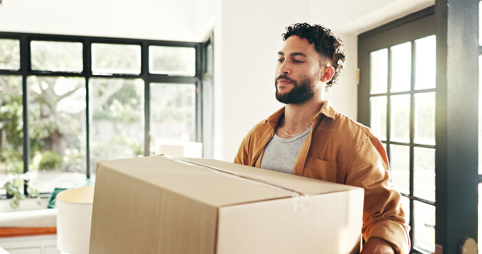 Man carrying a large box inside a bright room, representing 80 people sharing things they would never admit in real life