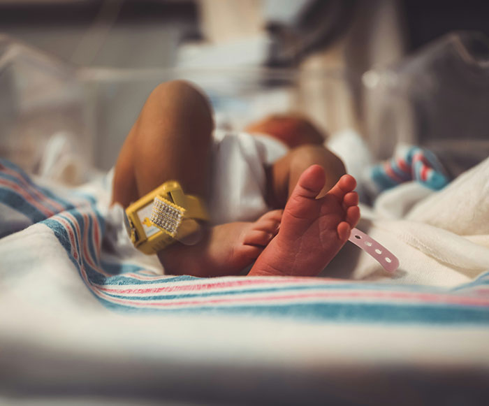 Newborn baby's feet with hospital ID bands in a crib, highlighting safe haven baby box and Kentucky cheerleader case. Newborn baby's feet with hospital ID bands in a crib, highlighting safe haven baby box and Kentucky cheerleader case.
