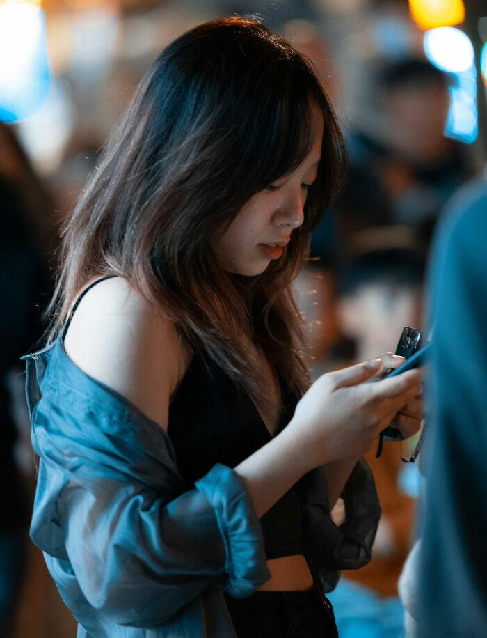 Young woman focused on her phone in a crowded setting, illustrating people saying out-of-touch things concept.