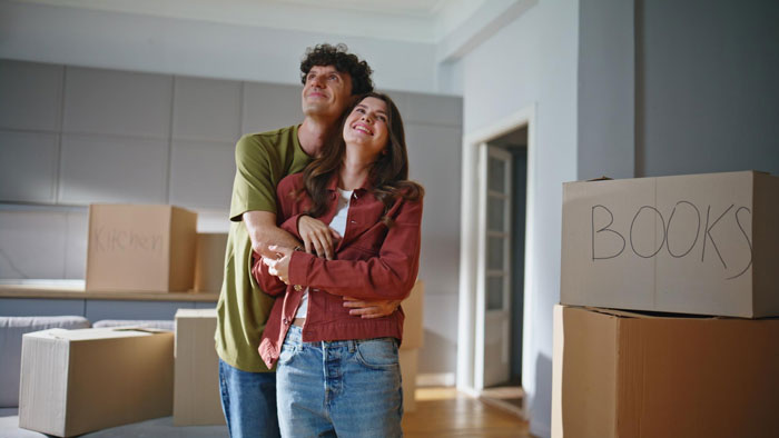 Young couple unpacking boxes in new home, unaware of nosy neighbor trauma lurking nearby in the quiet neighborhood. Young couple unpacking boxes in new home, unaware of nosy neighbor trauma lurking nearby in the quiet neighborhood.