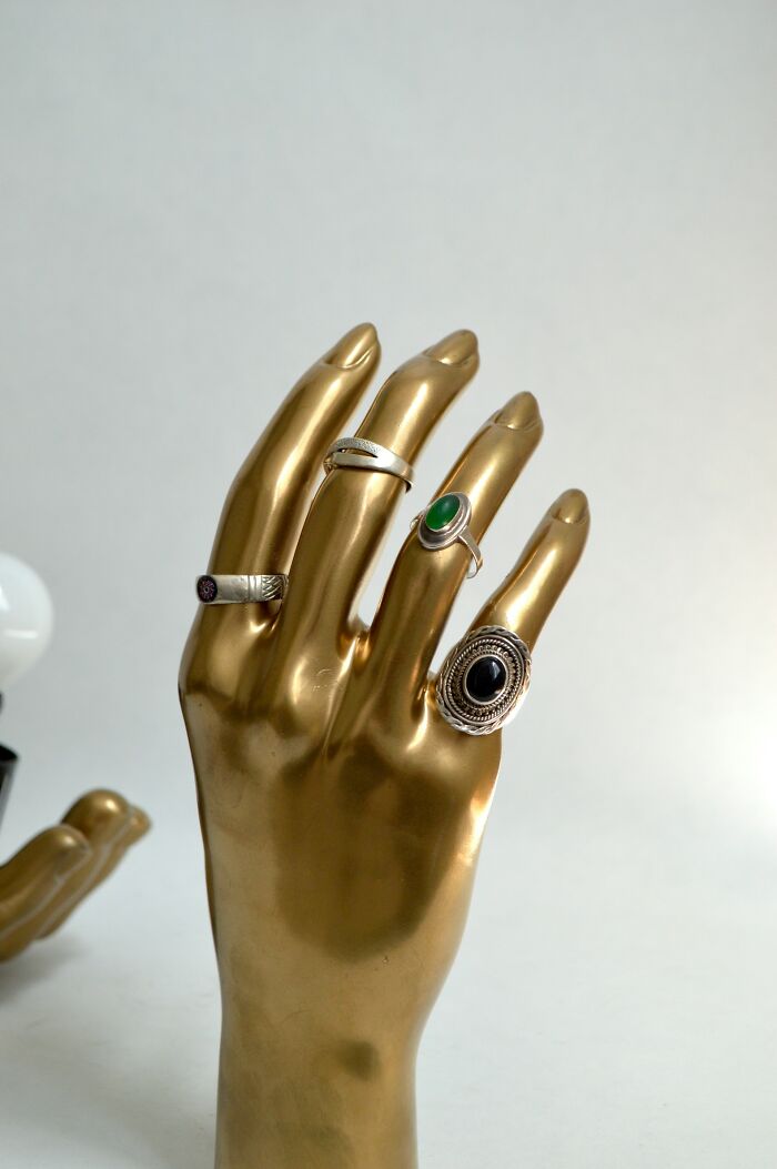 Golden hand display with silver rings featuring green and black stones, evoking creepy stories to tell in dark woods atmosphere.