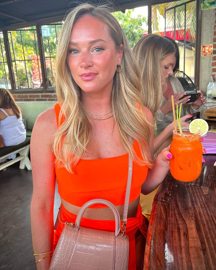 Young woman in an orange outfit holding a drink, related to nurse suspended for calling out doctor's sick remark.