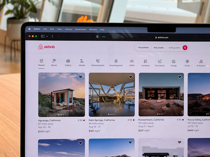 Airbnb listings on laptop screen with various vacation rentals displayed, woman worried about creepy host texts.