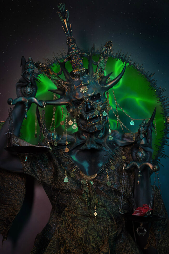 Haunting Halloween character with intricate skull makeup, adorned with gold chains and dark horns against a green background.