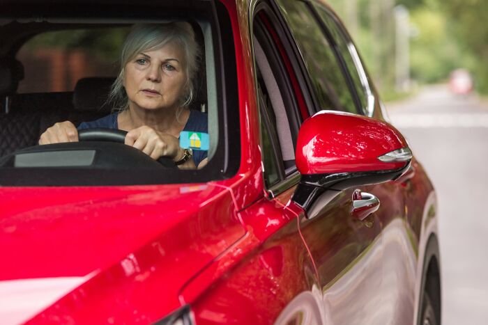 Older woman looking worried while sitting inside a red car, illustrating innocent people blamed by police in wrongful cases.