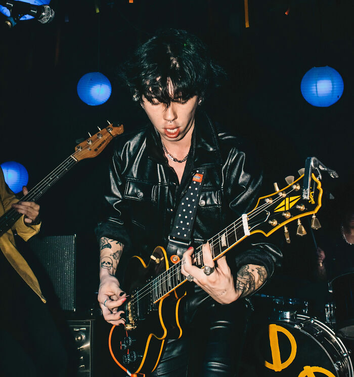 Musician playing electric guitar on stage with tattoos and leather jacket, representing professions not seen as relationship material.