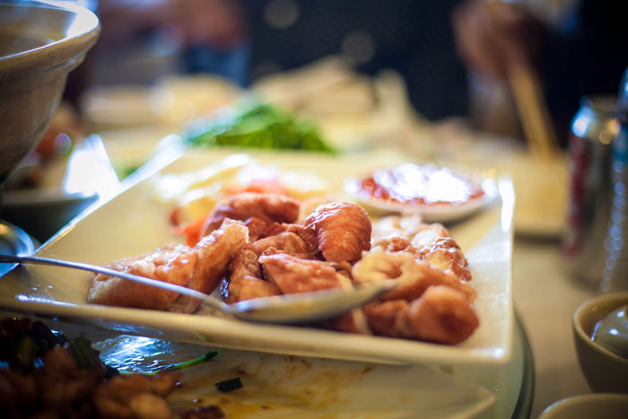 Plate of fried pork intestine served with dipping sauce on a table with chopsticks in a dining setting.