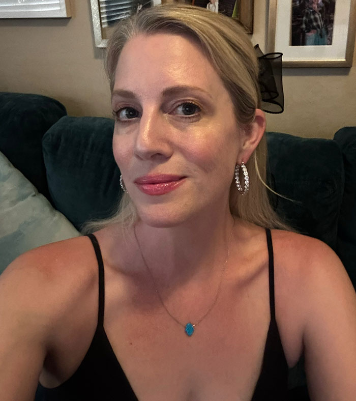 Woman with blonde hair and hoop earrings taking a selfie, reflecting shock after friendship ends over mom shorts.