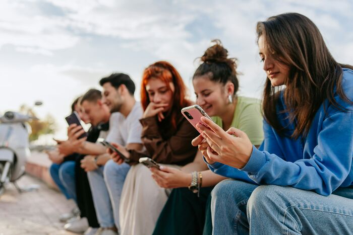 Group of Gen Z individuals sitting outside, each focused on their smartphones, reflecting Gen Z clients troubling behavior. Group of Gen Z individuals sitting outside, each focused on their smartphones, reflecting Gen Z clients troubling behavior.