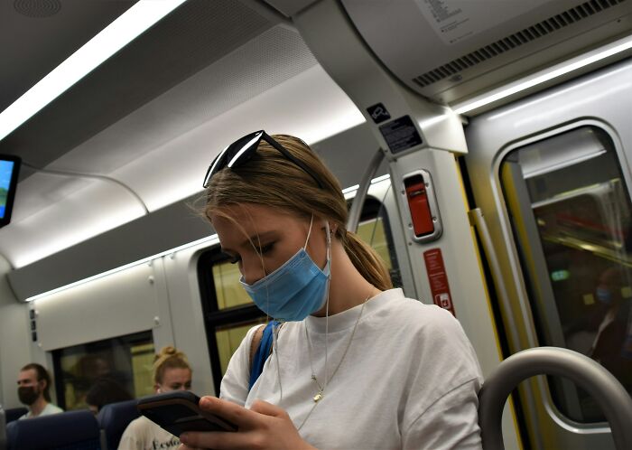 Young woman wearing a mask on public transit, focusing on her phone, illustrating Gen Z clients troubling behavior concept. Young woman wearing a mask on public transit, focusing on her phone, illustrating Gen Z clients troubling behavior concept.