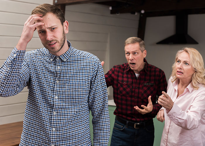 Stressed young man being confronted by older couple, illustrating parents made son raise siblings and turned against him.