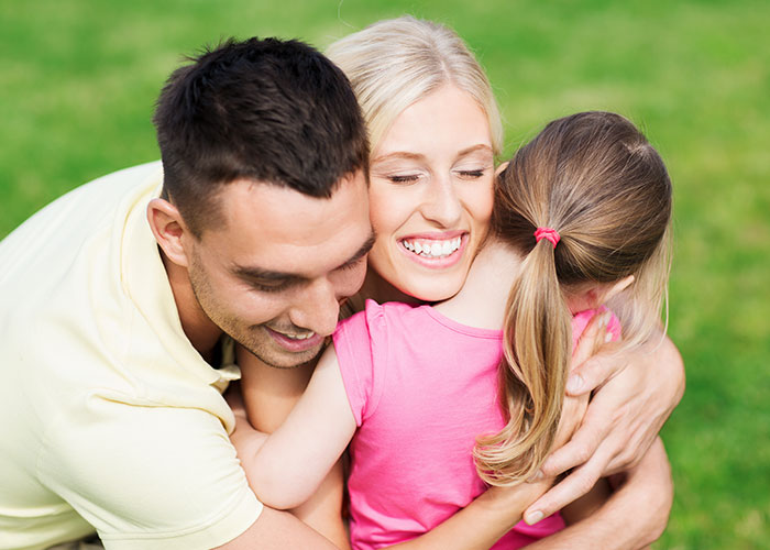 Young adult son hugging siblings outdoors, reflecting parents made him raise younger siblings and family struggles.