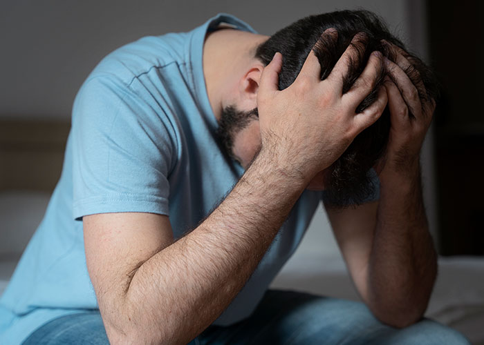 Young adult male stressed and overwhelmed sitting with head in hands, representing son raising his younger siblings.