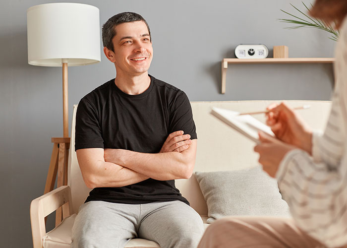 Young man in casual clothes sitting during a therapy session, reflecting on raising younger siblings and family struggles.