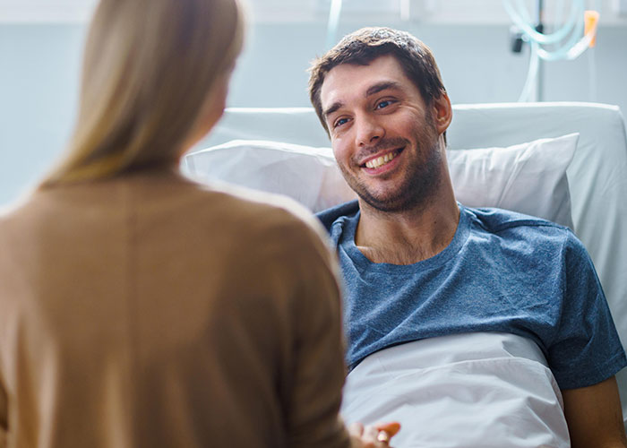 Young man in hospital bed smiling at woman, representing parents made son raise his younger siblings story.